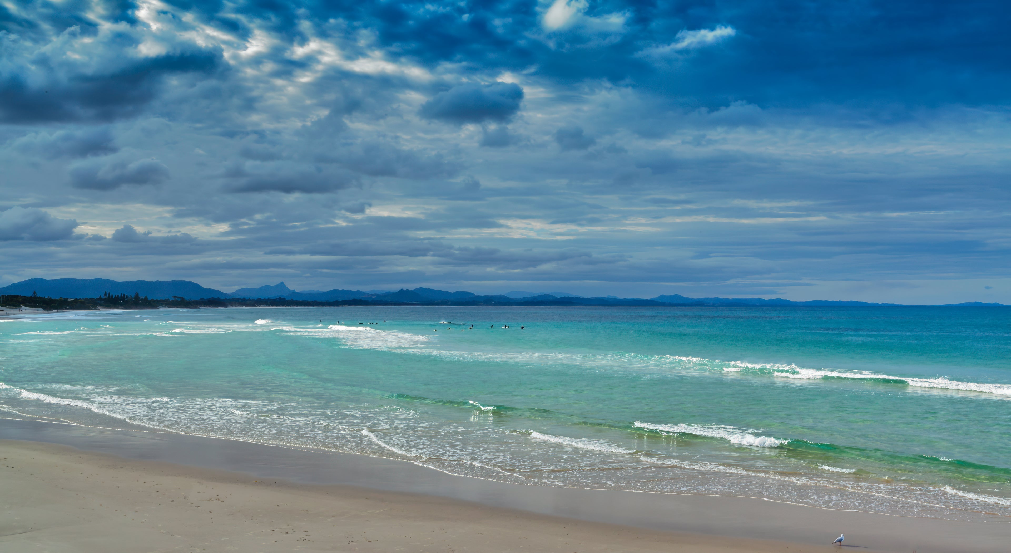 Byron Bay beach with dark skies forming over surfers enjoying the afternoon sun and emerald green waters as the clouds roll in