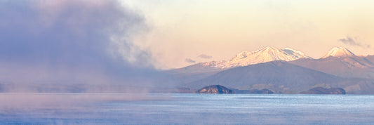 Panoramic view of a mountain range with snow peaks over a body of water.