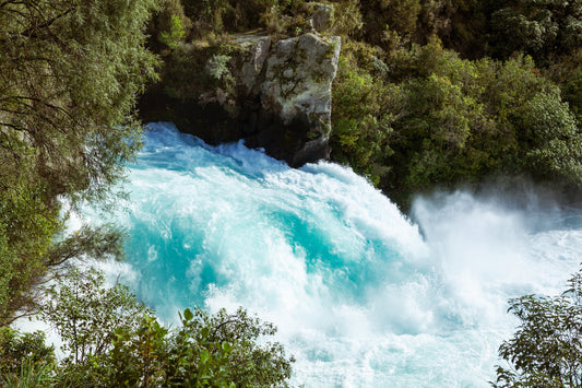 Rushing turquoise waterfall surrounded by lush green trees and rocky cliffs.
